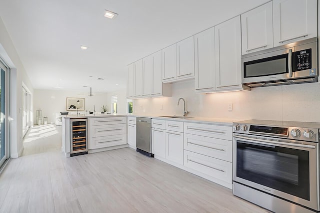 kitchen featuring appliances with stainless steel finishes, sink, white cabinets, wine cooler, and kitchen peninsula