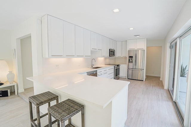 kitchen featuring white cabinetry, appliances with stainless steel finishes, a kitchen bar, and kitchen peninsula