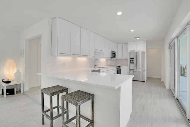 kitchen with a breakfast bar, white cabinetry, light hardwood / wood-style flooring, kitchen peninsula, and stainless steel appliances