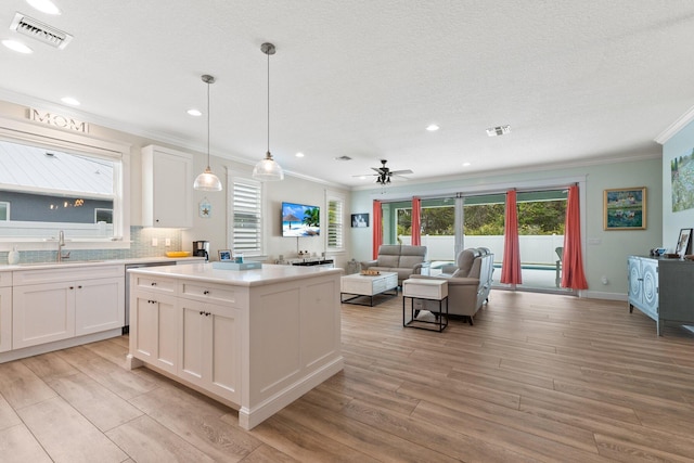 kitchen with white cabinetry, sink, hanging light fixtures, a center island, and crown molding