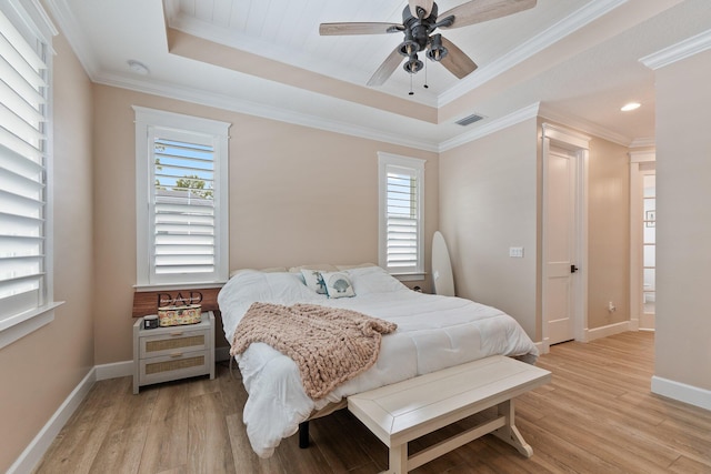 bedroom with a raised ceiling, crown molding, light wood-type flooring, and multiple windows