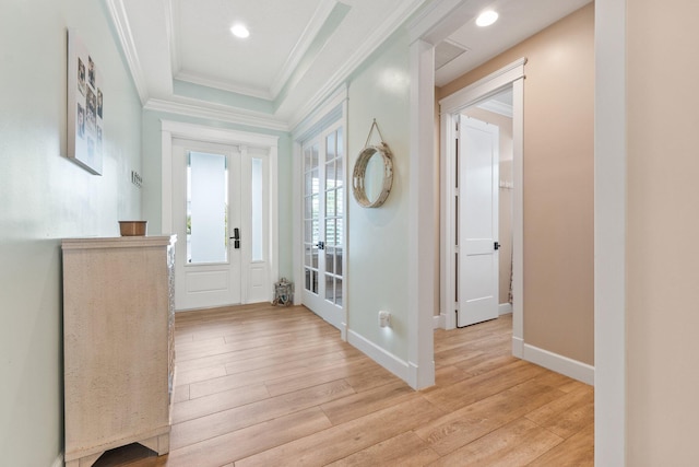 foyer entrance featuring a raised ceiling, ornamental molding, light hardwood / wood-style floors, and french doors