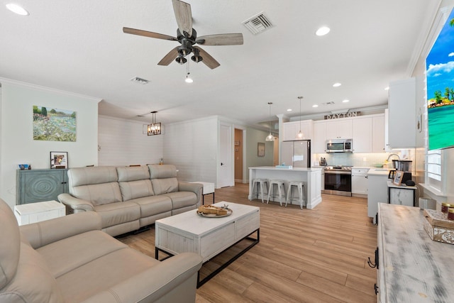 living room with sink, ceiling fan with notable chandelier, ornamental molding, and light hardwood / wood-style floors