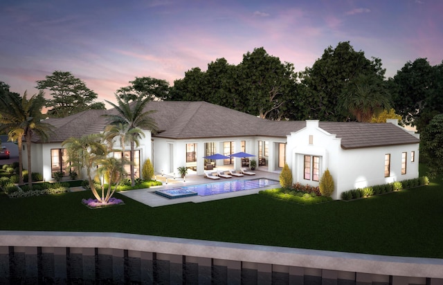 back house at dusk featuring a fenced in pool, a lawn, and a patio area