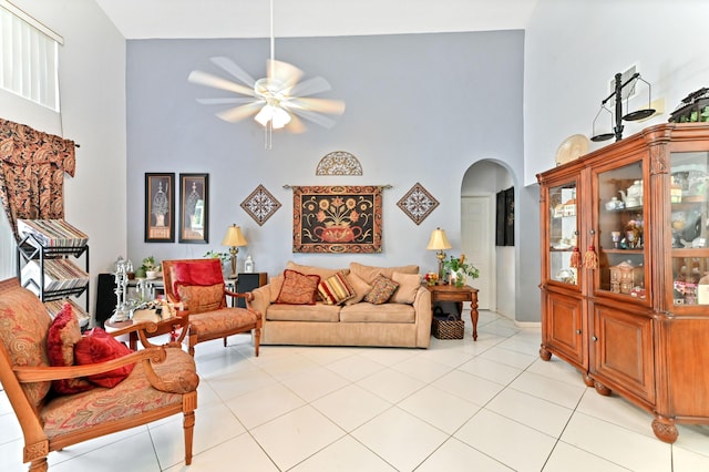 living area with arched walkways, a towering ceiling, a ceiling fan, and light tile patterned flooring