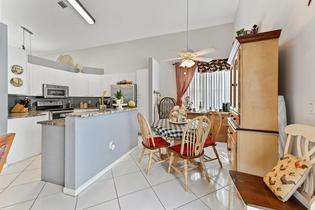 kitchen featuring white cabinetry, lofted ceiling, dark stone countertops, light tile patterned floors, and stainless steel appliances