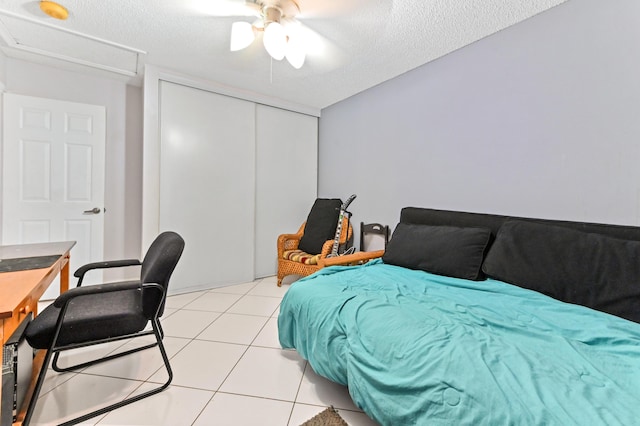 bedroom with light tile patterned floors, a closet, a ceiling fan, a textured ceiling, and attic access