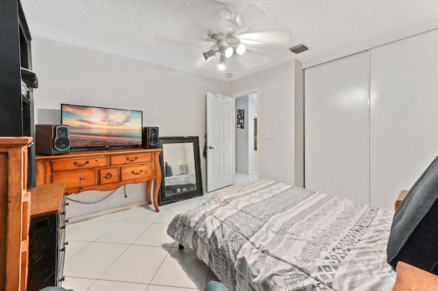 bedroom with a closet, light tile patterned floors, a textured ceiling, visible vents, and ceiling fan