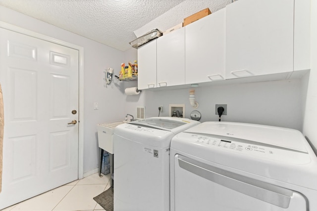 washroom featuring a textured ceiling, separate washer and dryer, light tile patterned floors, and cabinet space