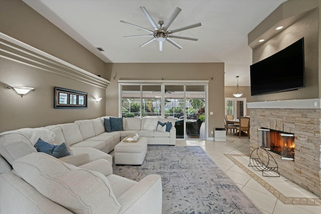 living room with light tile patterned flooring, ceiling fan, and a stone fireplace