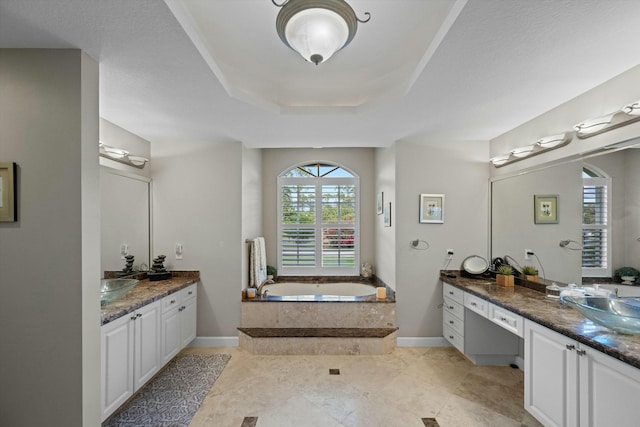 bathroom featuring vanity, a raised ceiling, and tiled tub