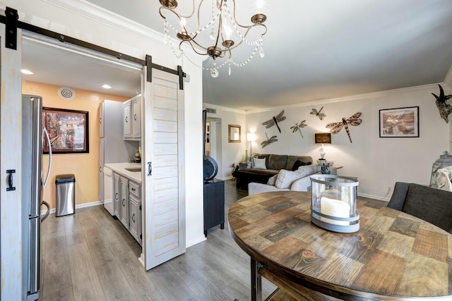 dining area with ornamental molding, a barn door, and light wood-type flooring