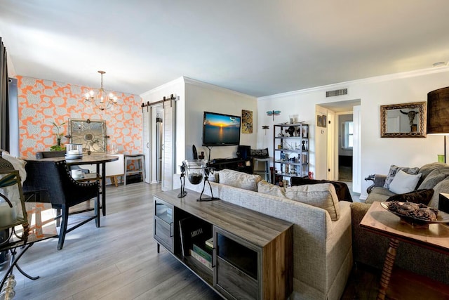 living room featuring crown molding, a barn door, a chandelier, and light wood-type flooring