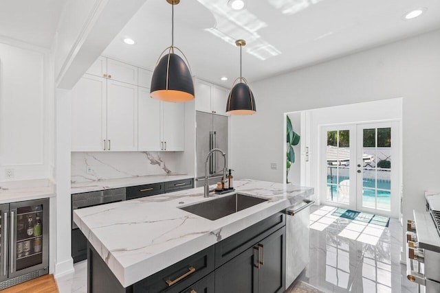 kitchen with sink, white cabinetry, hanging light fixtures, beverage cooler, and a kitchen island with sink