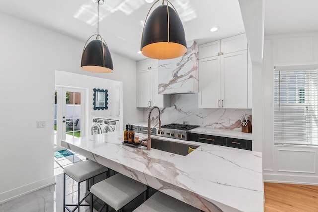 kitchen featuring washing machine and clothes dryer, a center island, pendant lighting, light stone countertops, and white cabinets