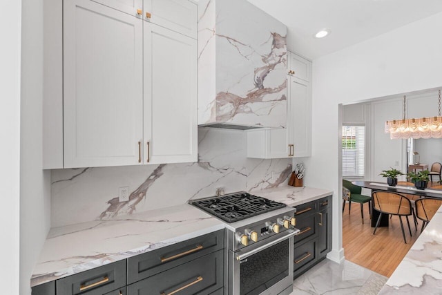 kitchen featuring wall chimney exhaust hood, white cabinetry, tasteful backsplash, decorative light fixtures, and stainless steel stove