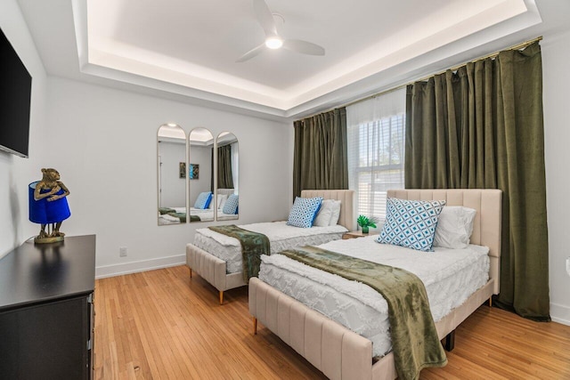 bedroom featuring ceiling fan, a tray ceiling, and light hardwood / wood-style floors