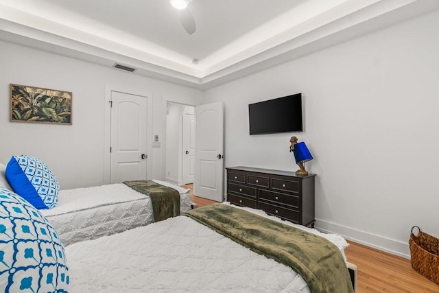 bedroom with ceiling fan, a tray ceiling, and hardwood / wood-style floors