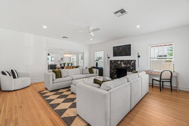 living room with a wealth of natural light, ceiling fan with notable chandelier, and light wood-type flooring