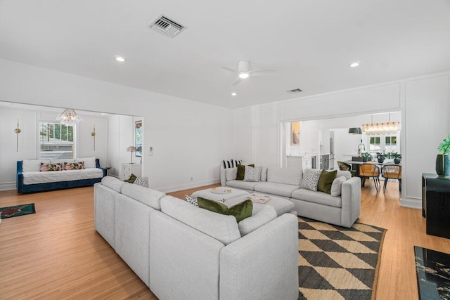 living room with ceiling fan with notable chandelier and light wood-type flooring