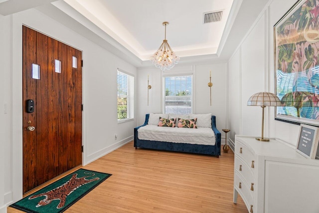 foyer entrance with light hardwood / wood-style flooring, an inviting chandelier, and a tray ceiling