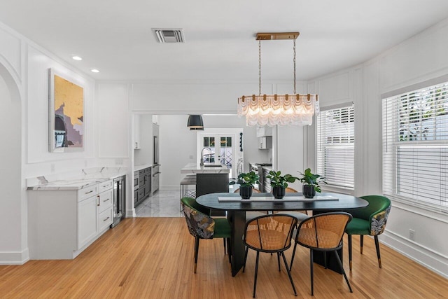 dining room featuring a healthy amount of sunlight, beverage cooler, and light hardwood / wood-style flooring