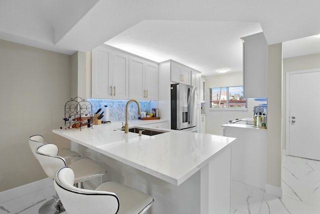 kitchen with sink, a breakfast bar area, stainless steel fridge, kitchen peninsula, and white cabinets