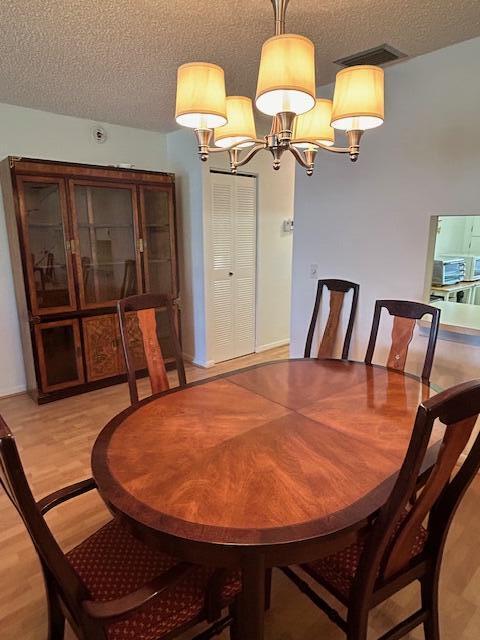 dining space with light wood-style flooring, visible vents, a chandelier, and a textured ceiling