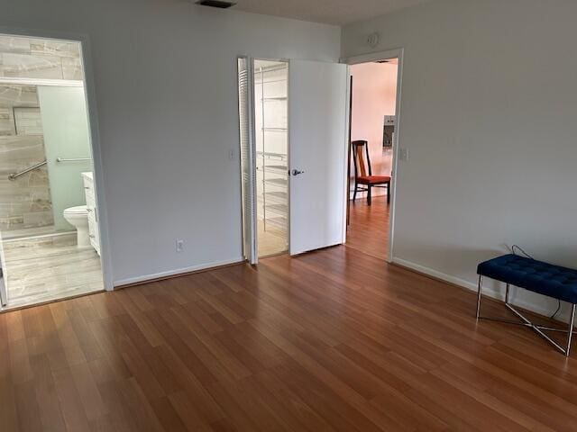 unfurnished bedroom featuring dark wood-style flooring, visible vents, ensuite bath, and baseboards