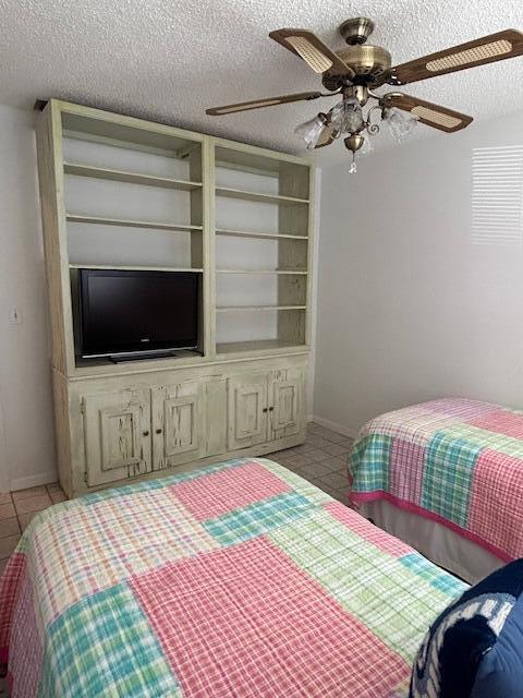 bedroom with ceiling fan, baseboards, a textured ceiling, and light tile patterned flooring