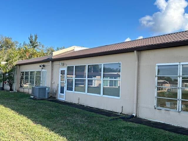 back of property with a lawn, cooling unit, and a tiled roof