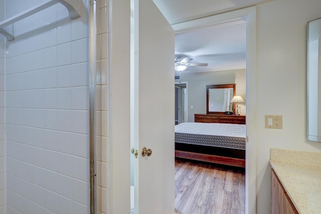 bathroom with hardwood / wood-style floors, vanity, ceiling fan, walk in shower, and a textured ceiling