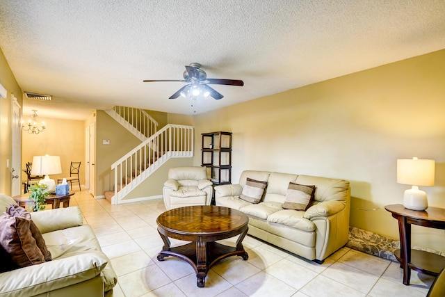 tiled living room with ceiling fan with notable chandelier and a textured ceiling