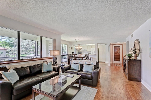 living room with a textured ceiling, a notable chandelier, and light wood-type flooring