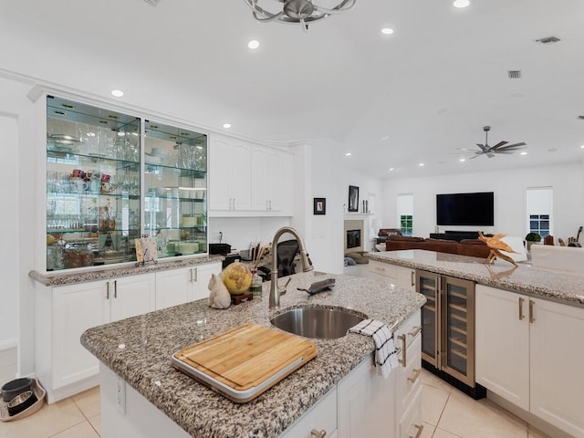 kitchen featuring sink, a kitchen island with sink, white cabinetry, wine cooler, and light stone counters