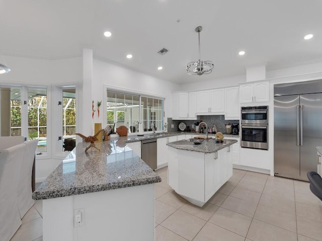 kitchen featuring stainless steel appliances, a kitchen island, light stone counters, and decorative light fixtures