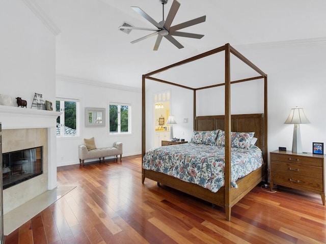 bedroom featuring crown molding, ceiling fan, hardwood / wood-style floors, and a tile fireplace