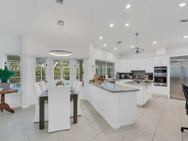 kitchen featuring pendant lighting, white cabinetry, kitchen peninsula, stainless steel appliances, and light stone countertops