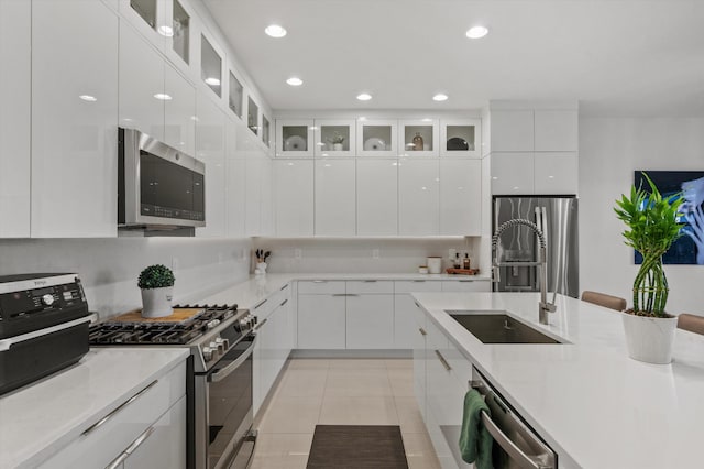 kitchen with sink, white cabinetry, light tile patterned floors, stainless steel appliances, and backsplash