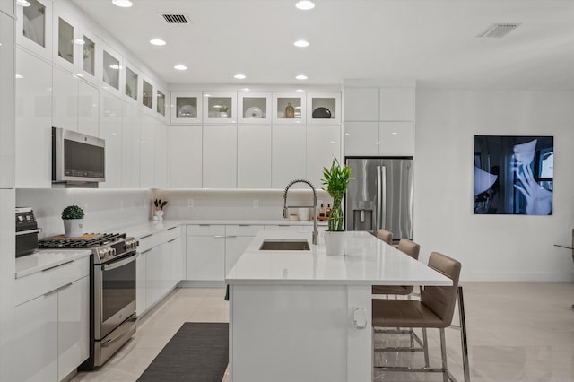 kitchen with an island with sink, appliances with stainless steel finishes, white cabinets, and a kitchen bar