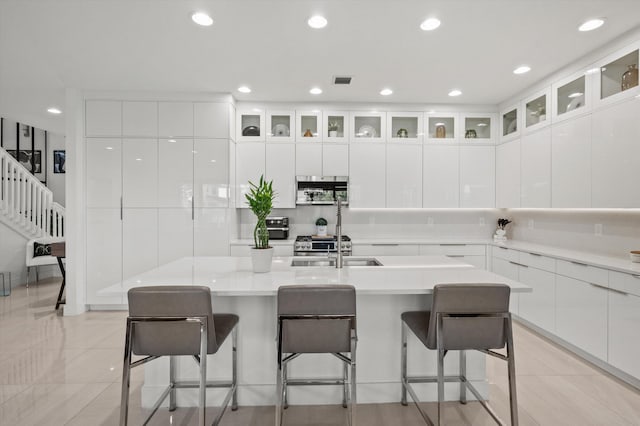 kitchen with a breakfast bar area, an island with sink, and white cabinets