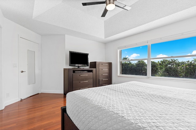 bedroom featuring hardwood / wood-style flooring, ceiling fan, a raised ceiling, and a textured ceiling