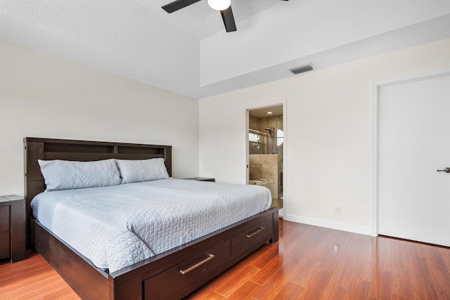 bedroom featuring ceiling fan, ensuite bath, light hardwood / wood-style floors, and a textured ceiling