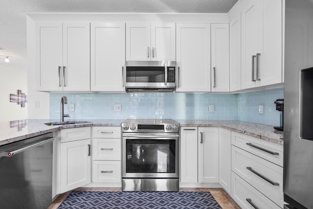 kitchen with white cabinetry, appliances with stainless steel finishes, sink, and light stone counters