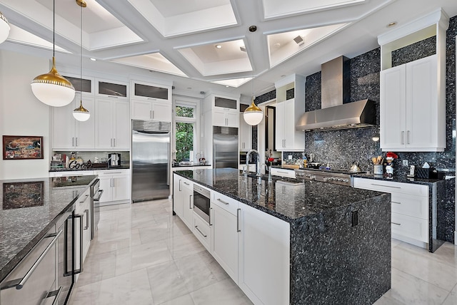 kitchen with a large island, coffered ceiling, wall chimney range hood, decorative backsplash, and built in appliances