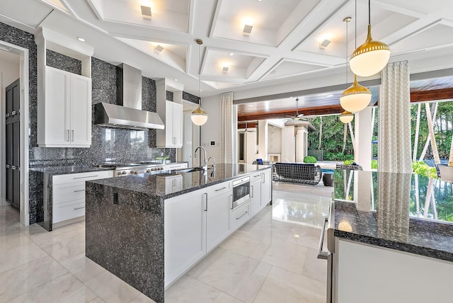 177 Commodore Dr, Jupiter, FL 33477 - kitchen with wall chimney exhaust hood, stainless steel microwave, a center island with sink, decorative backsplash, and white cabinetry