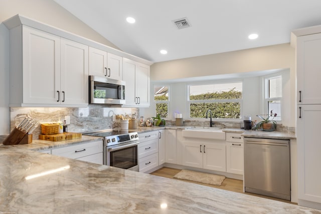 kitchen featuring sink, stainless steel appliances, light stone countertops, white cabinets, and vaulted ceiling