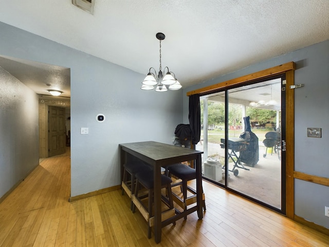 dining space with an inviting chandelier, a textured ceiling, and light wood-type flooring