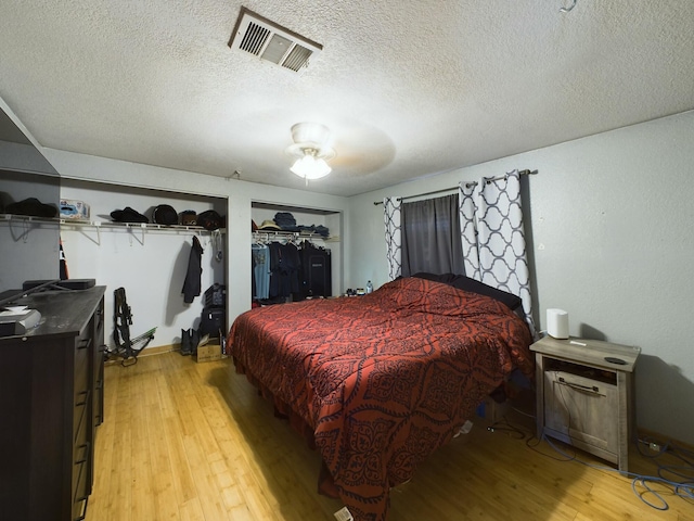bedroom with ceiling fan, two closets, a textured ceiling, and light hardwood / wood-style floors