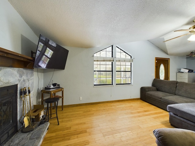 living room with a stone fireplace, vaulted ceiling, a textured ceiling, ceiling fan, and light hardwood / wood-style floors